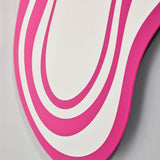 Close-up of Nimbus Pink Banded Glass Wall Mirror, irregular cloud-like outline with concentric pink and mirrored glass bands, frameless, against a plain grey wall.