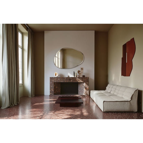 Frameless organic-shaped wall mirror with bevelled edge, 136cm, mounted above a marble fireplace in a living room with a cream sofa and terrazzo floor.