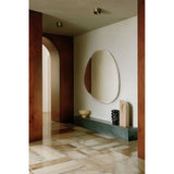 Pure Bevelled Edge Organic Wall Mirror 136cm, frameless irregular-shaped glass with bevelled edge, mounted on a wall above a dark console table in a hallway setting.