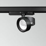 The Helionis LED Track Round Spotlight 22W 3000K in black, featuring a sleek circular design, is installed on a ceiling rail. Its adjustable head directs the light downward, showcasing the bulb within the fixture. A minimalist light gray background accentuates its energy efficiency.