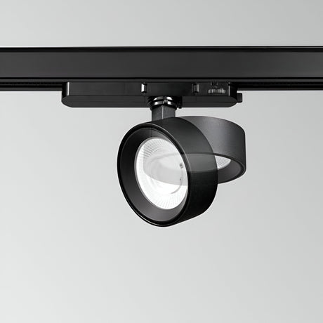 The Helionis LED Track Round Spotlight 22W 3000K in black, featuring a sleek circular design, is installed on a ceiling rail. Its adjustable head directs the light downward, showcasing the bulb within the fixture. A minimalist light gray background accentuates its energy efficiency.