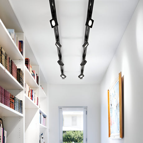A modern hallway with white walls and a light wooden floor is decorated with bookshelves filled with books on the left and a framed picture on the right wall. The ceiling is enhanced by integrated LED technology featuring the Helionis LED Track Square Spotlight 22W 3000K in black, while a window at the end provides a view of greenery outside.