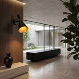 A modern, minimalist interior with the sleek Funk Wall Light - Black, wooden paneling, a dark vase on a stone bench, a large plant, and floor-to-ceiling windows overlooking a lush courtyard.