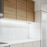 A modern kitchen with light wood cabinets and sleek appliances, including a refrigerator and an oven. The countertops are white, complemented by a glossy backsplash. Bright, minimalistic lighting features the Nocturne LED Wall Light 7W 3000K - White, 50cm with aluminium construction.