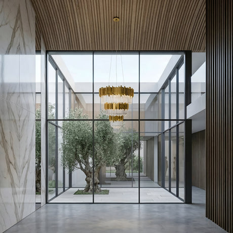 Niori Royal 30-Light Tiered Crystal Chandelier in gold hanging from a wood-slat ceiling above a glass-walled courtyard with olive trees and marble walls.