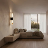 Minimalist bedroom with neutral tones, low bed, floating nightstand, beige bedding, wooden floors, large window with white curtains and greenery view, accented by the Fiora LED Alabaster Wall Light in Matte Black & Soft White.