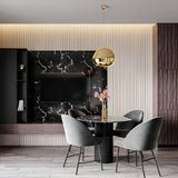 Modern dining area with a round black marble table, four gray upholstered chairs, a gold Lava Small LED Pendant Light with adjustable cable, and a wall-mounted TV on a black marble accent wall with wood paneling and ambient lighting.