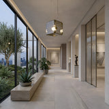 Modern hallway features floor-to-ceiling windows, potted plants, sculptures, and abstract art. City skyline and greenery shine outside, while the Qbic LED Large Pendant Light - Clear adds a touch of elegance with its modern design inside.