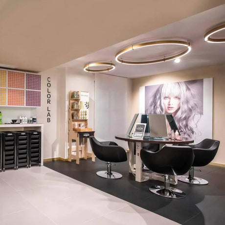 Orbita 116cm LED ceiling light in bronze-gold metal, a large circular flush fitting shown above a salon styling area with black chairs and a round table.