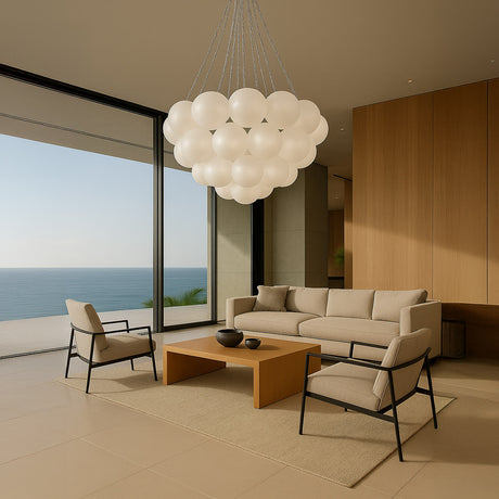 A modern living room with ocean views, neutral furniture, a wooden coffee table, and the Orb 17 Light Cluster Suspension - Silver featuring frosted white glass spheres hanging from the ceiling.
