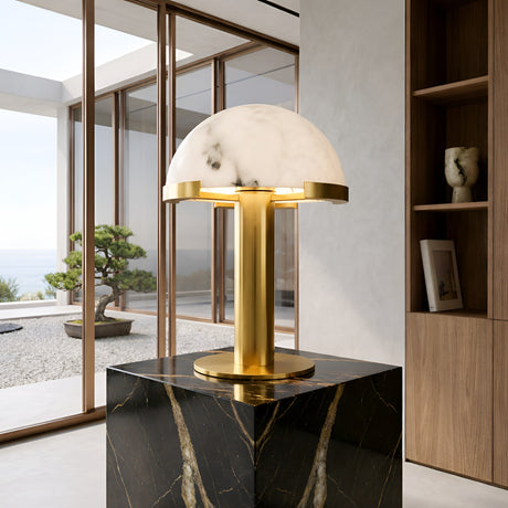 The Noctelis 1 Light Dome Alabaster Table Lamp in Soft White & Brass rests on a black marble pedestal in a minimalist room with large windows and scenic outdoor views.