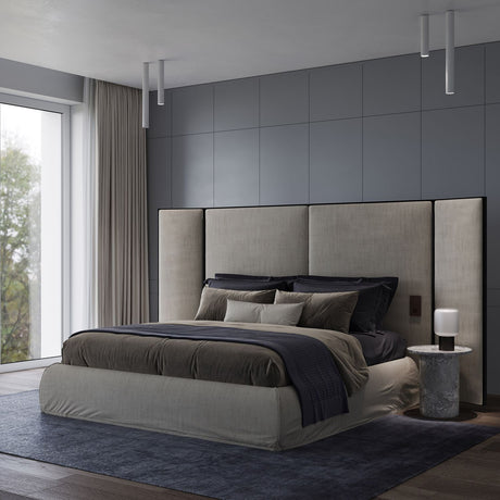 A modern bedroom exudes minimalist elegance with a large bed featuring gray and dark bedding. The tall, upholstered headboard complements the sleek design. Beside the bed sits a round nightstand with a lamp, while the Pulcra LED Tube Ceiling Light in white enhances the room's modern aesthetic. Walls and flooring have neutral tones, and a large window with sheer curtains lets in natural light.