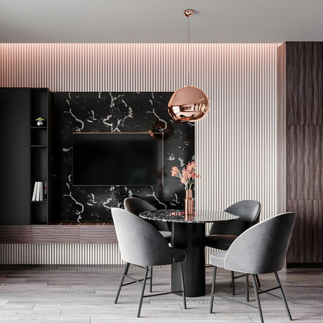 A modern dining area features a round black marble table, four gray upholstered chairs, the Lava Small LED Pendant Light in copper, a TV on a black marble wall with vertical wood paneling, and soft ambient lighting.