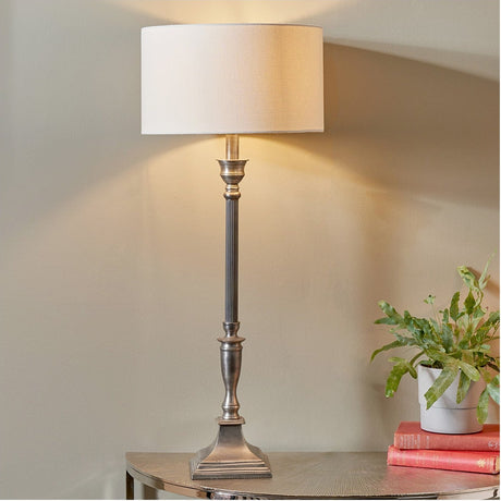 Canterbury Antique Silver Aluminium Table Lamp with fluted column base and cream drum shade, styled on a console table beside books and a potted plant.
