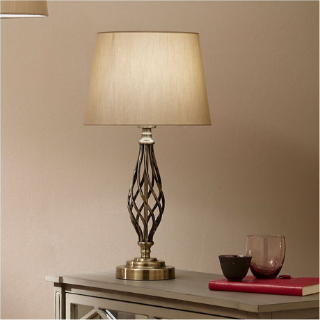 Jenna Antique Brass Gold Twist Detail Table Lamp with a spiral metal base and tapered fabric shade, styled on a sideboard beside a red book and glassware.