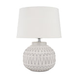 Anneli table lamp with a round ceramic base in warm white featuring an Aztec-style textured pattern, topped with a white linen tapered shade, on a plain white background.