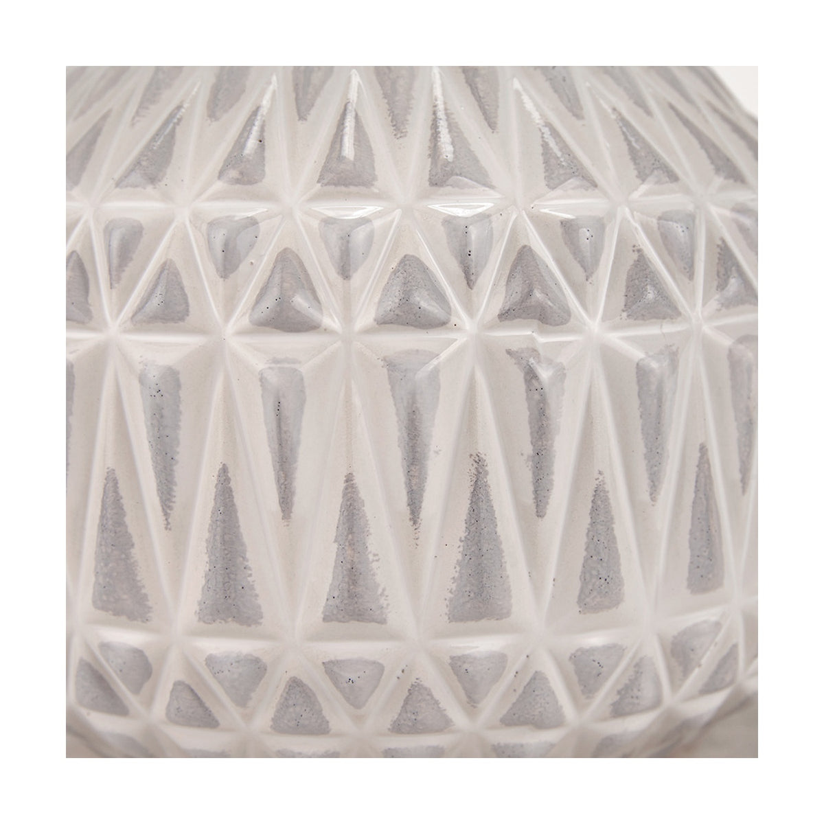 Close-up of the Anneli table lamp's ceramic base showing a faceted Aztec-style triangle texture in warm white with grey-shadowed recesses.