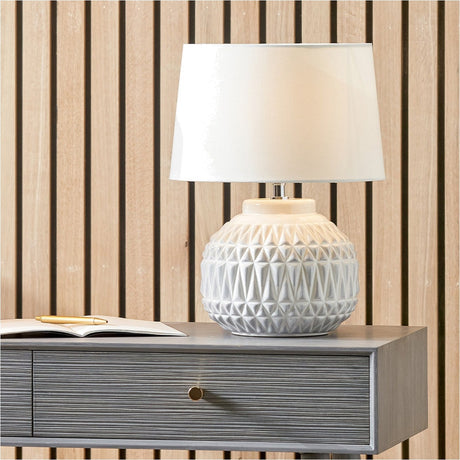 Anneli Warm White Aztec Texture Ceramic Table Lamp, 40cm, with geometric-textured white ceramic base and tapered white fabric shade, shown on a grey bedside table.