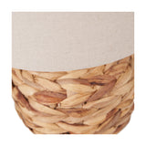 Close-up of the Zadi Table Lamp's natural plaited water hyacinth base beneath a plain oatmeal fabric shade, showing the woven texture in detail.