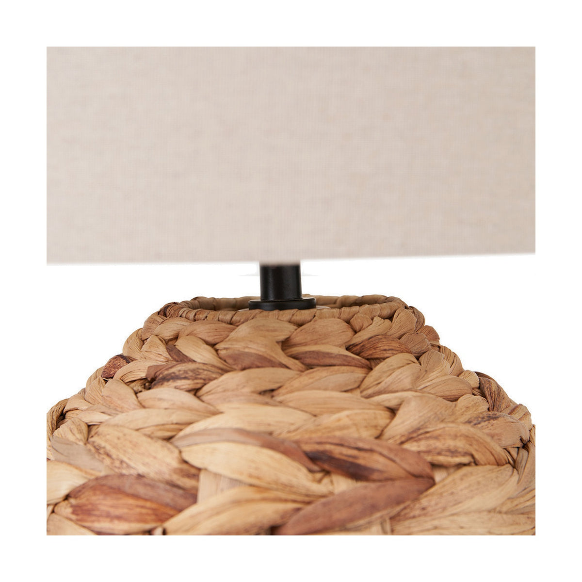 Close-up of the Zadi Natural Plaited Water Hyacinth Table Lamp, showing the braided natural woven base and black fitting beneath a neutral fabric shade.