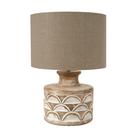Kingsbury table lamp with a carved wood base in white wash finish featuring a scalloped pattern, paired with a taupe linen drum shade, on a plain white background.