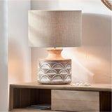 Kingsbury table lamp with carved white wash wood base and scallop pattern, paired with a natural linen drum shade, styled on a wooden sideboard.