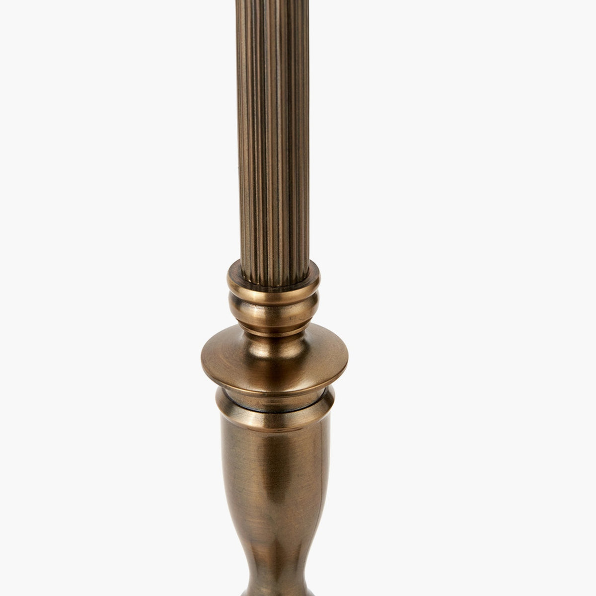 Close-up of the Canterbury Table Lamp Base's antique brass column with fluted detailing above a turned urn-shaped body, set against a plain white background.