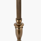 Close-up of the Canterbury Table Lamp Base's antique brass column with fluted detailing above a turned urn-shaped body, set against a plain white background.