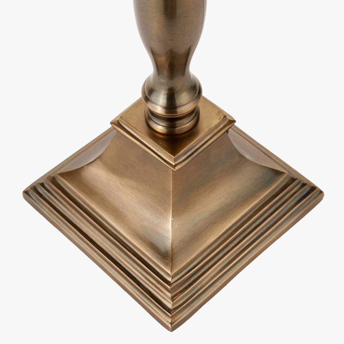 Close-up of the Canterbury Table Lamp Base's stepped square foot and turned column in antique brass, shown on a plain white background.