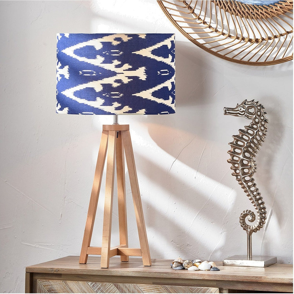 Whitby Wood Tapered 4 Post Table Lamp Base in natural wood with a navy and cream patterned drum shade, styled on a sideboard beside a metal seahorse ornament and shells.