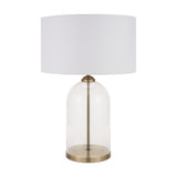 Cloche table lamp with a clear glass dome base, antique brass fittings and stem, and a white drum fabric shade, shown against a plain white background.