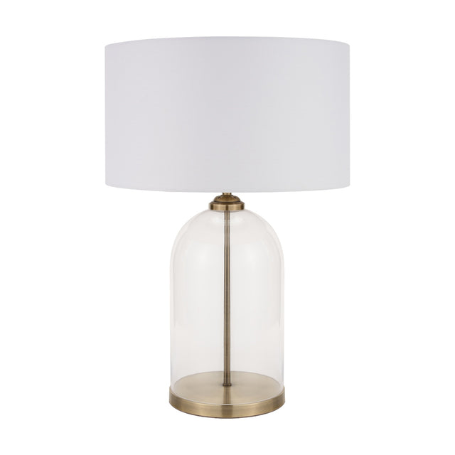 Cloche table lamp with a clear glass dome base, antique brass fittings and stem, and a white drum fabric shade, shown against a plain white background.