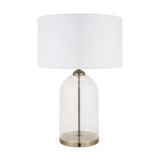 Cloche table lamp with a clear glass dome base, antique brass fittings and stem, and a white drum fabric shade, shown on a plain white background.