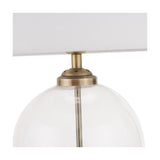 Close-up of the Cloche table lamp's antique brass fitting atop a clear glass globe base, with white fabric shade, against a plain white background.