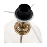 Close-up of the Cloche table lamp's antique brass gallery and black bulb holder, with white metal frame arms and clear glass shade visible against a white background.