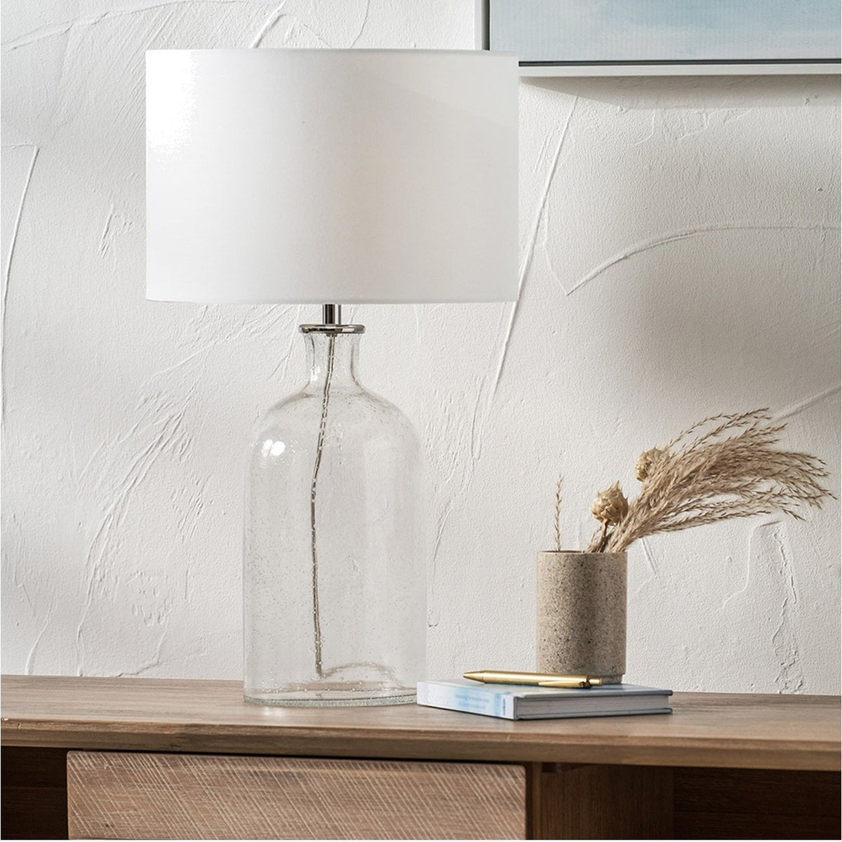 Bellamy Clear Bubble Glass Table Lamp, 53cm, with a white drum shade on a chrome fitting, styled on a wooden sideboard beside a vase and books.