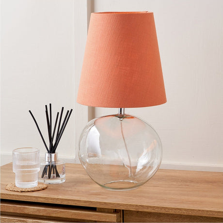 Hallie Clear Glass & Terracotta Shade Table Lamp, 43cm, with round glass base and linen shade, styled on a wooden sideboard beside a reed diffuser and glass tumbler.