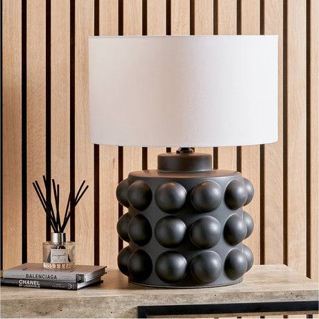 Serenity Black Bobbled Ceramic Large Table Lamp Base with white drum shade, styled on a wooden sideboard against a slatted wood panel wall.