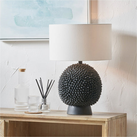 Wrenley Black Ceramic Sea Urchin Table Lamp Base, 37cm, with textured spiked sphere base and white drum shade, styled on a wooden sideboard.