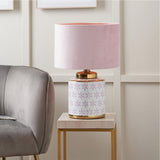 Thea Lilac & Gold Leaf ceramic table lamp with pink velvet drum shade, floral-patterned base and gold trims, shown on a marble side table in a living room setting.