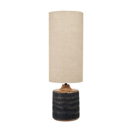 Alaric table lamp with a carved antique black wash mango wood base and tall cylindrical natural linen shade, shown on a plain white background.