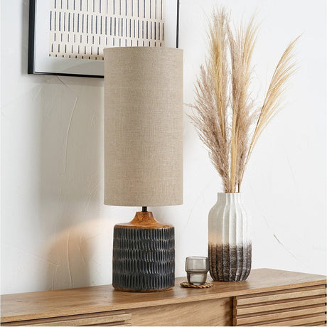 Alaric Antique Black Wash Mango Table Lamp, 77cm, with a tall cylindrical linen shade and textured mango wood base, styled on a wooden sideboard beside a ribbed vase and framed artwork.