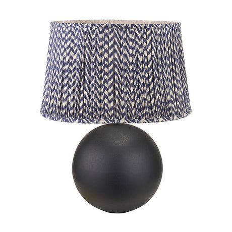 Benio table lamp with a matt black spherical metal base and a pleated drum shade in blue and cream chevron fabric, shown on a plain white background.