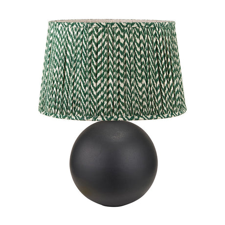 Benio table lamp with a matt black spherical metal base and a pleated forest green and cream herringbone fabric drum shade, shown on a plain white background.