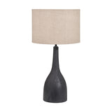 Corella Black Mango curved table lamp base with a bottle-shaped wooden body, paired with a neutral drum shade, set against a plain white background.