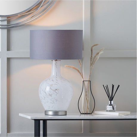 Aurora Speckled White Glass Table Lamp, 58cm, with grey drum shade and brushed metal base, styled on a marble table beside a vase and dried grasses.