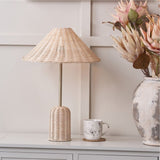 Hali Rattan Base & Shade Table Lamp, 53cm, with woven rattan cone shade and cylindrical base on a brass stem, shown on a console table with a marble mug and vase of flowers.