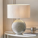 Mabel Silver Dot Textured Ceramic Table Lamp with an oval fabric shade, shown on a console table in a neutral-toned living room setting.