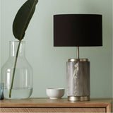 Carrara grey marble effect ceramic table lamp, 50cm, with a cylindrical marbled base, brushed metal fittings and a black drum shade, shown on a wooden sideboard.