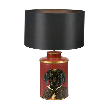 Table lamp with red hand-painted metal base featuring a dachshund in a coat, gold trim, and black silk drum shade, on a plain white background.
